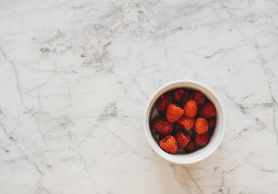 a white marble table with a white ramekin with raspberries 