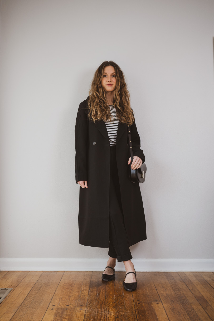 outfit idea with a black trench coat, striped tee, black tapered pants, and black mary jane flats