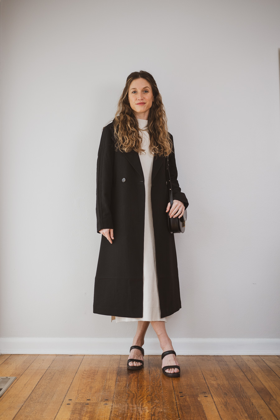 outfit idea with a black trench coat, beige knit midi dress, and black heeled sandals