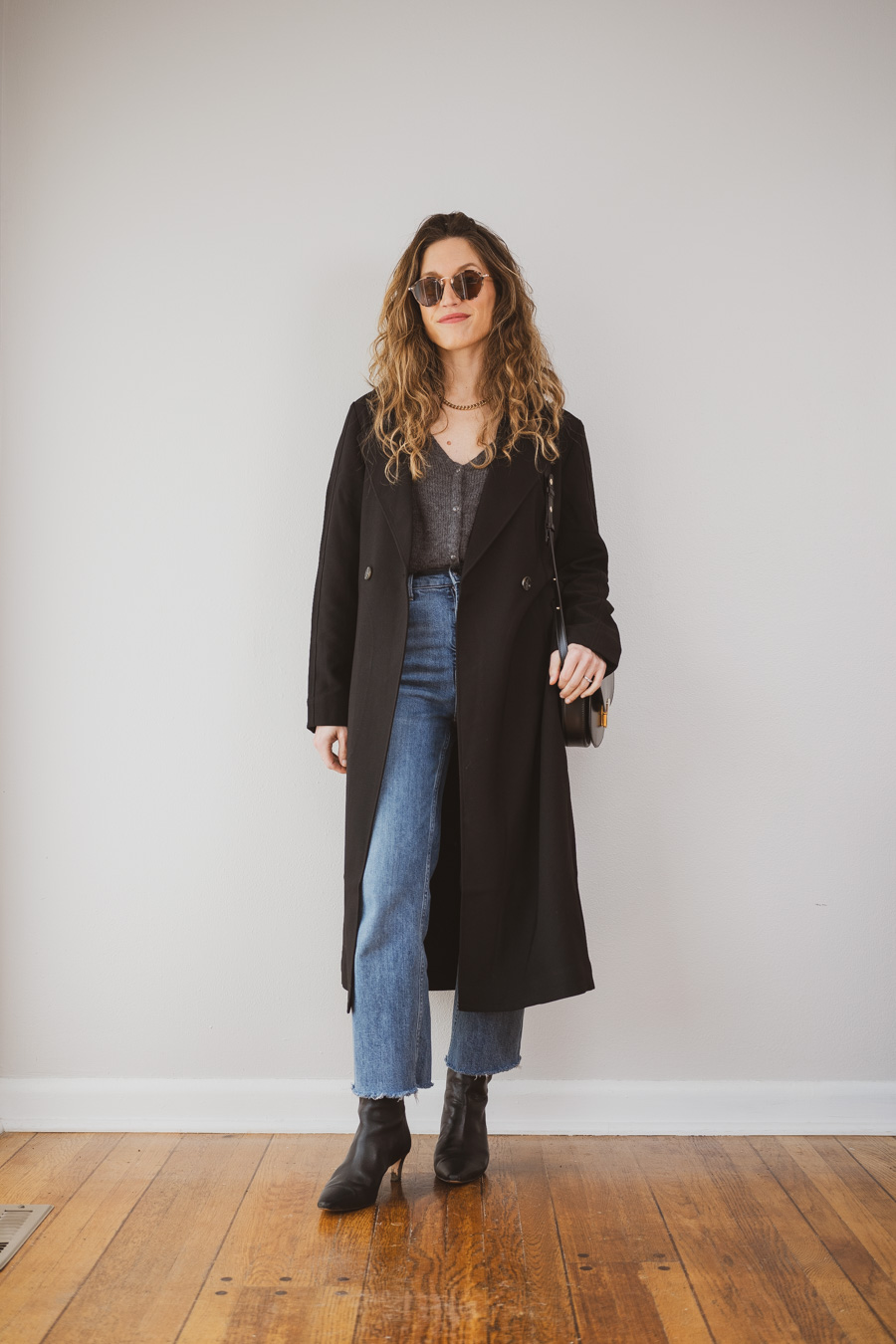 outfit with a black trench coat, gray sweater cardigan, medium wash cropped straight jeans, and black heeled ankle boots