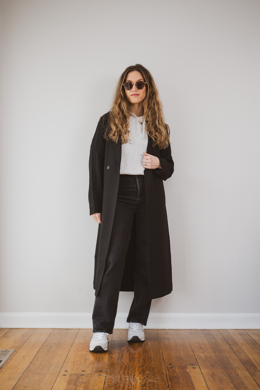 black trench coat with a gray hoodie, black straight leg jeans, and New Balance sneakers