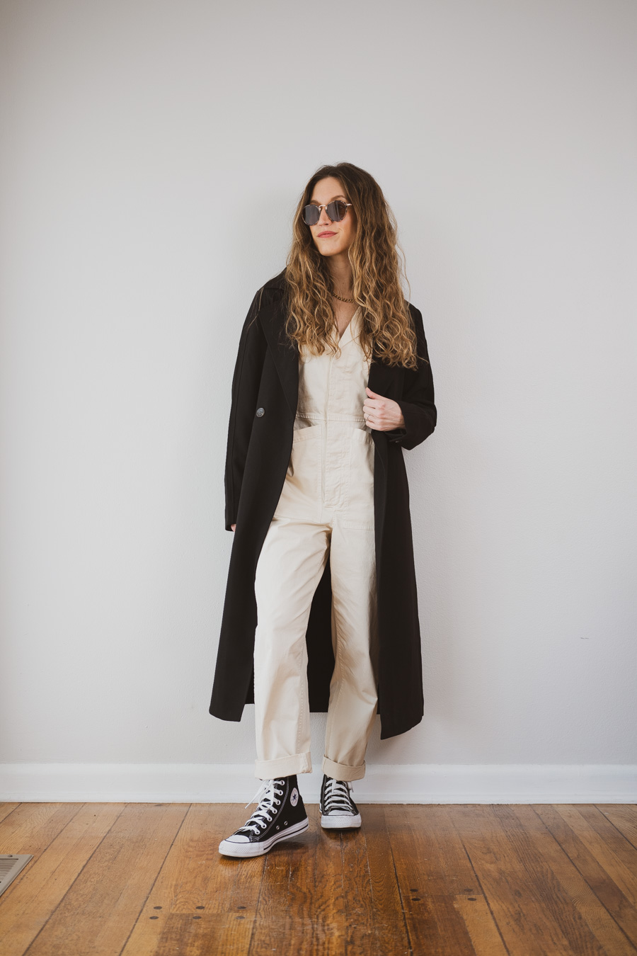 black trench coat outfit idea with an ivory jumpsuit and high top Converse