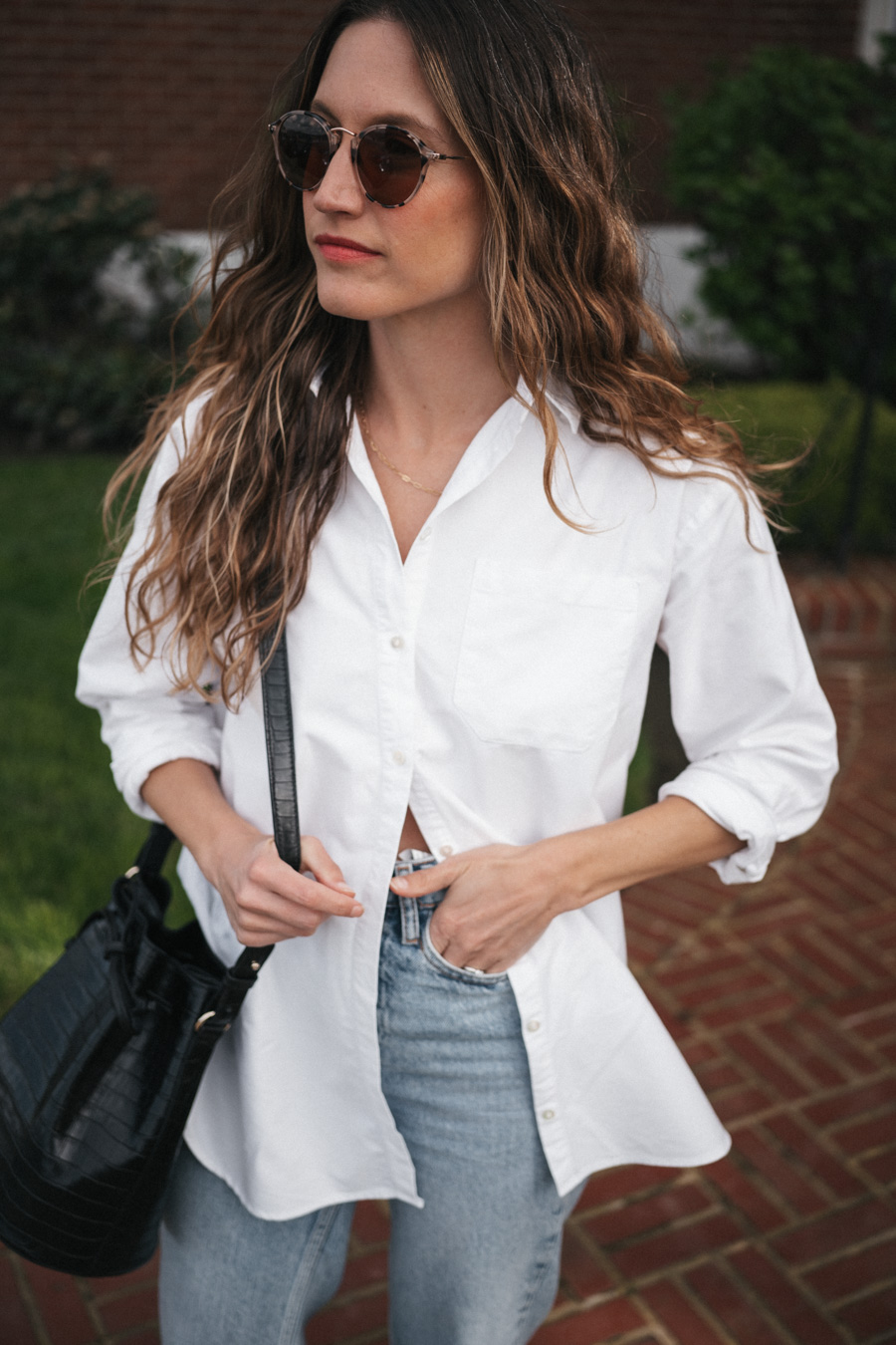 ashley wearing the Sézane Max Shirt in white, light wash cuffed jeans, black fisherman sandals, and round tortoiseshell frame sunglasses and a black crocodile print bucket bag