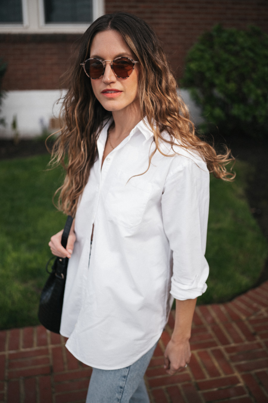 ashley wearing the Sézane Max Shirt in white, light wash cuffed jeans, black fisherman sandals, and round tortoiseshell frame sunglasses and a black crocodile print bucket bag