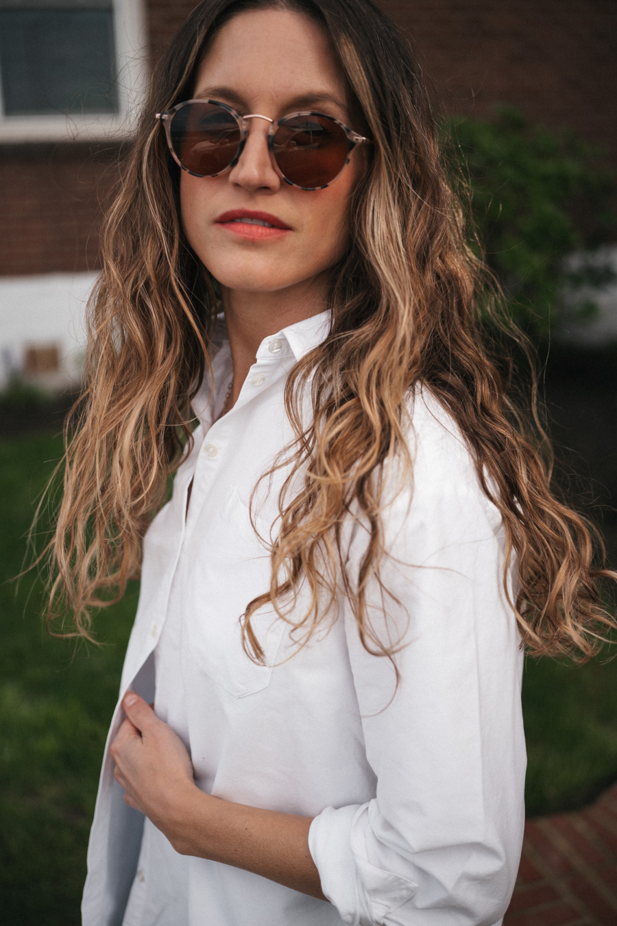 ashley wearing the Sézane Max Shirt in white, light wash cuffed jeans, black fisherman sandals, and round tortoiseshell frame sunglasses and a black crocodile print bucket bag