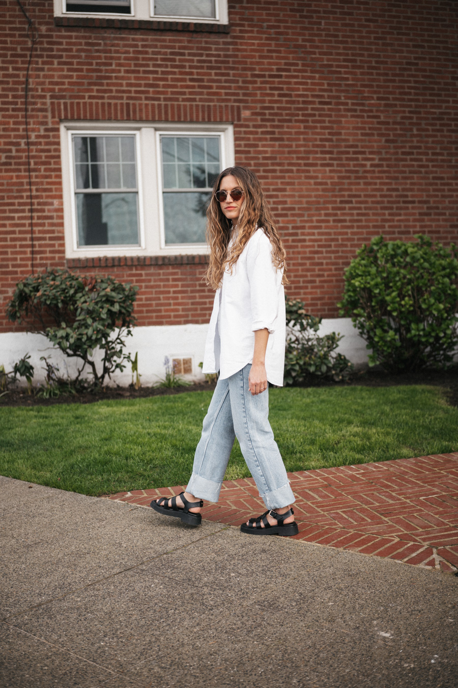 ashley wearing the Sézane Max Shirt in white, light wash cuffed jeans, black fisherman sandals, and round tortoiseshell frame sunglasses and a black crocodile print bucket bag