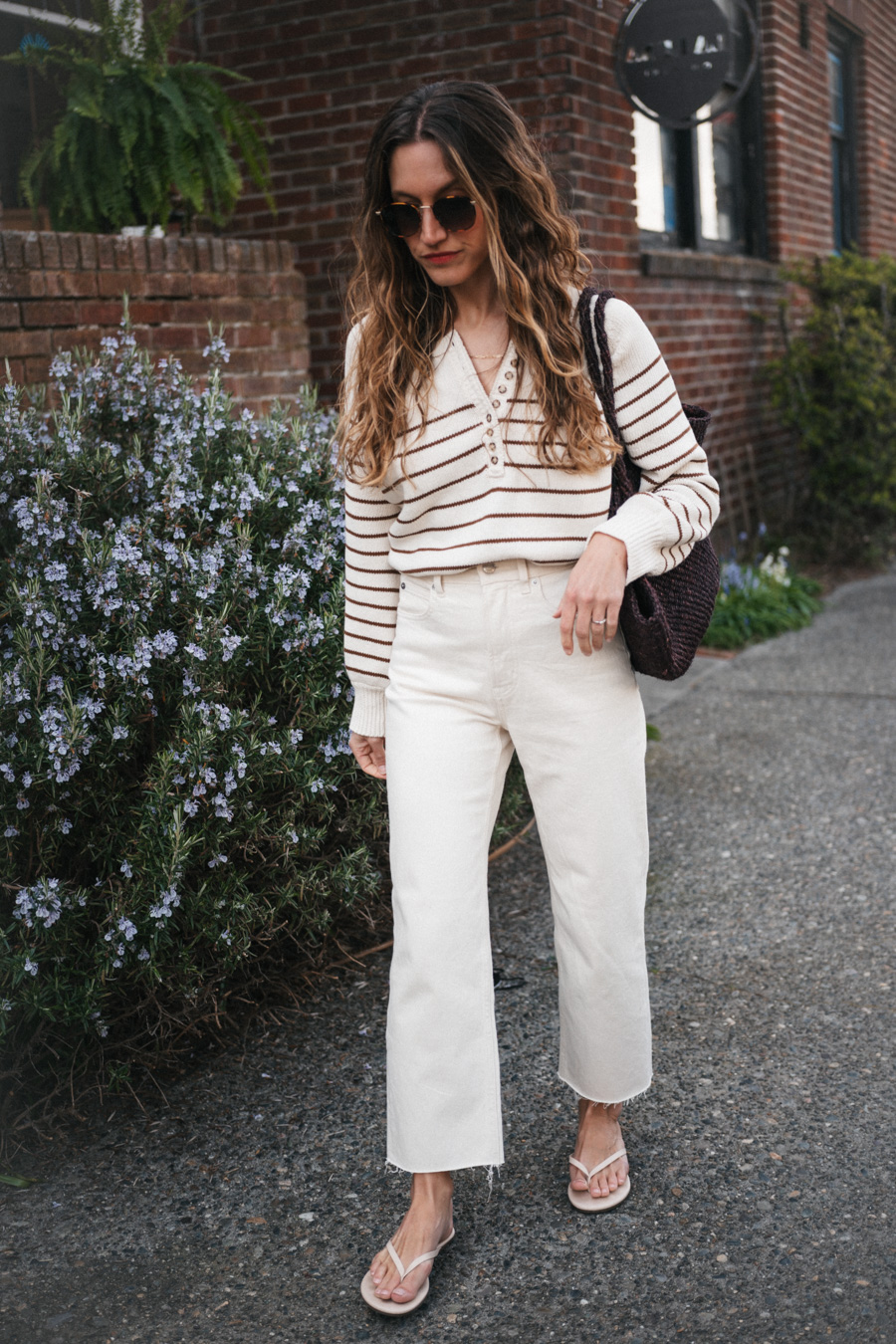 ashley wearing the Sézane Léontine Jumper with white denim, ivory sandals, and a brown woven tote bag