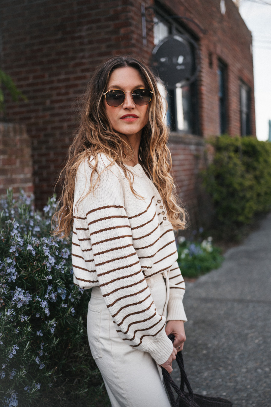 ashley wearing the Sézane Léontine Jumper with white denim, ivory sandals, and a brown woven tote bag