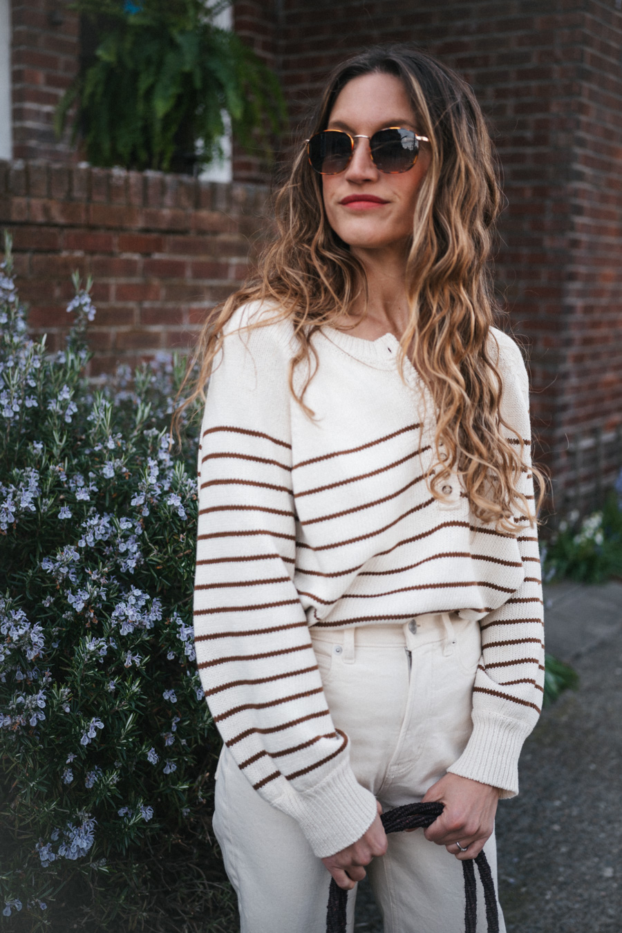 ashley wearing the Sézane Léontine Jumper with white denim, ivory sandals, and a brown woven tote bag