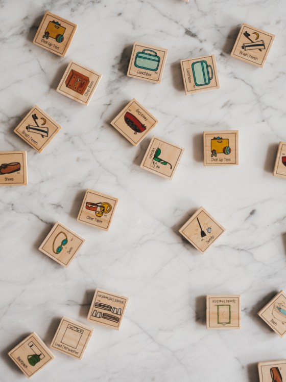 wood tiles with different chores pictured on them spread on a white marble table