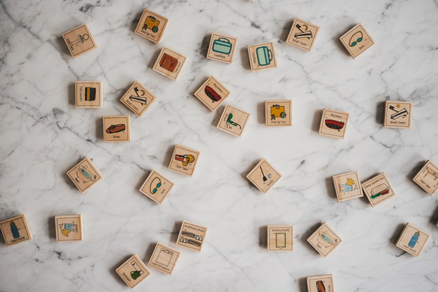 wood tiles with different chores pictured on them spread on a white marble table