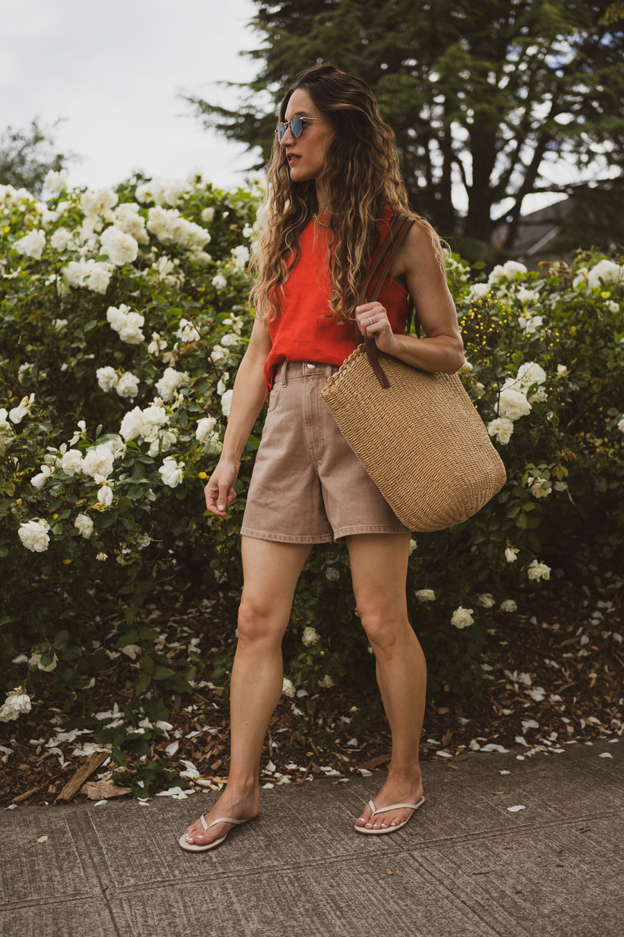 fourth of july outfit idea with a red tank, tan denim short, beige sandals, and a straw tote bag