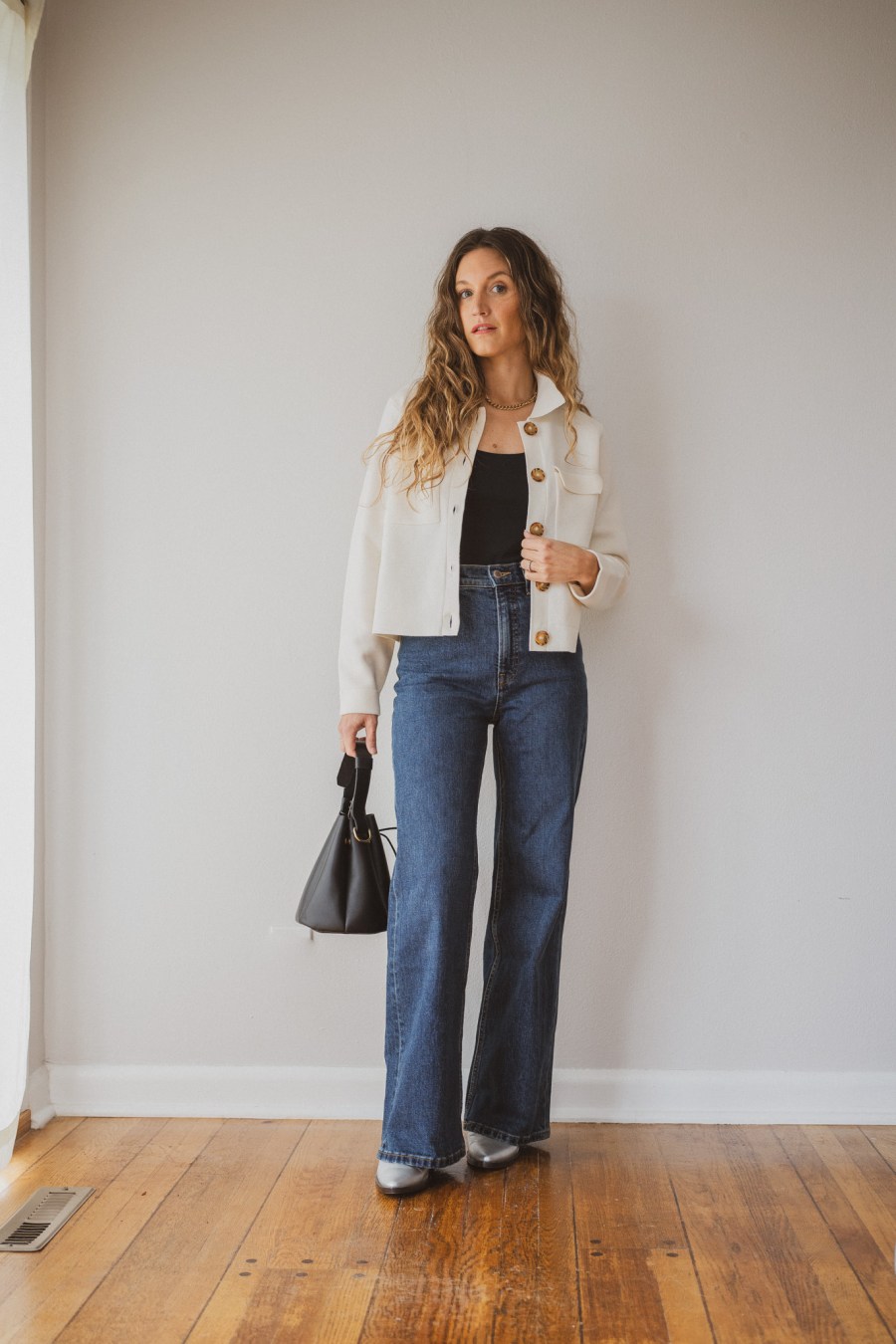 Sézane Betty Cardigan outfit idea with a black bodysuit layered underneath, dark wash wide leg jeans, silver boots, and a black bucket bag