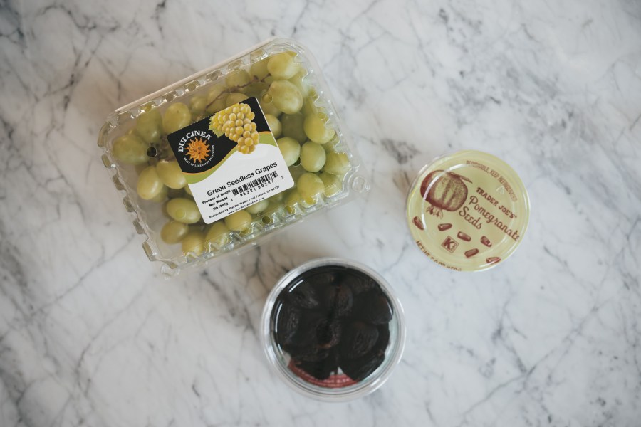 a white marble table with grapes, pomegranate seeds, and dried figs for a holiday charcuterie board