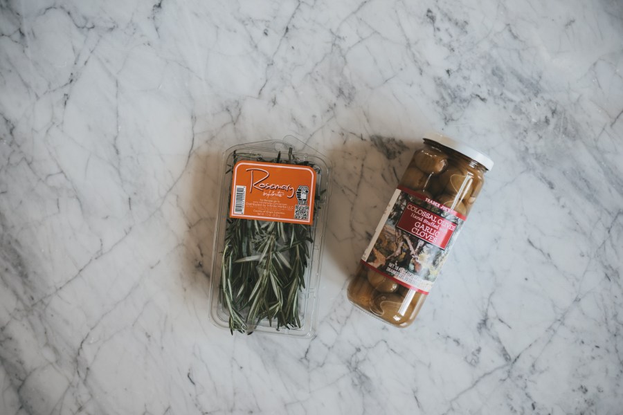 a white marble table with fresh rosemary and garlic stuffed olives for a holiday charcuterie board