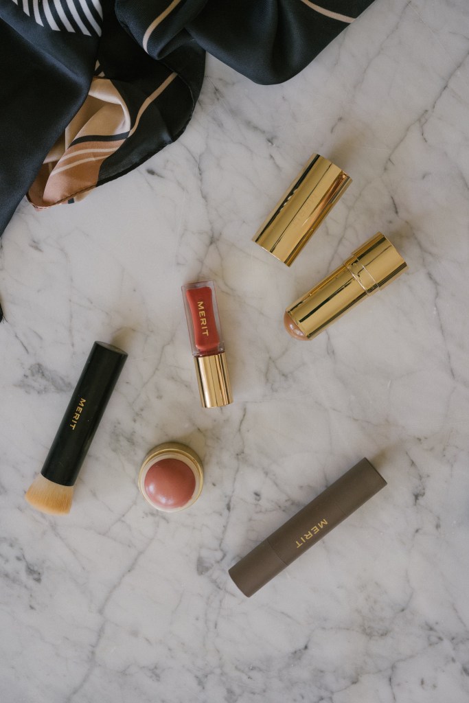 merit beauty products on a marble table with a black and beige patterned scarf