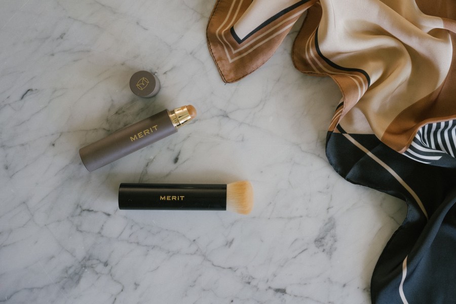 merit beauty products on a marble table with a black and beige patterned scarf