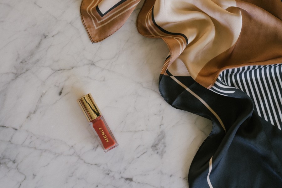 merit beauty products on a marble table with a black and beige patterned scarf