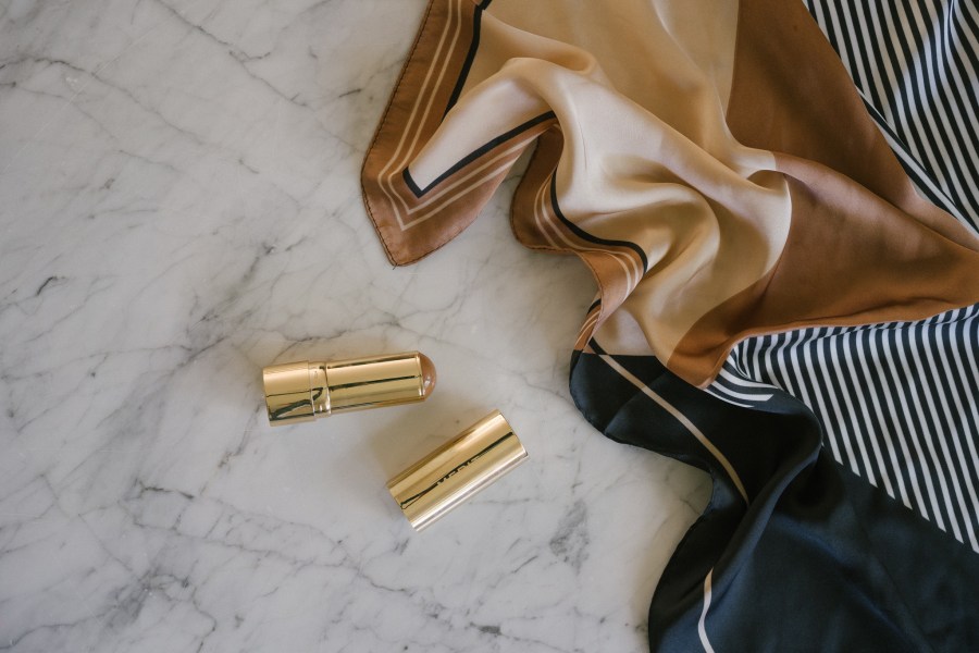 merit beauty products on a marble table with a black and beige patterned scarf