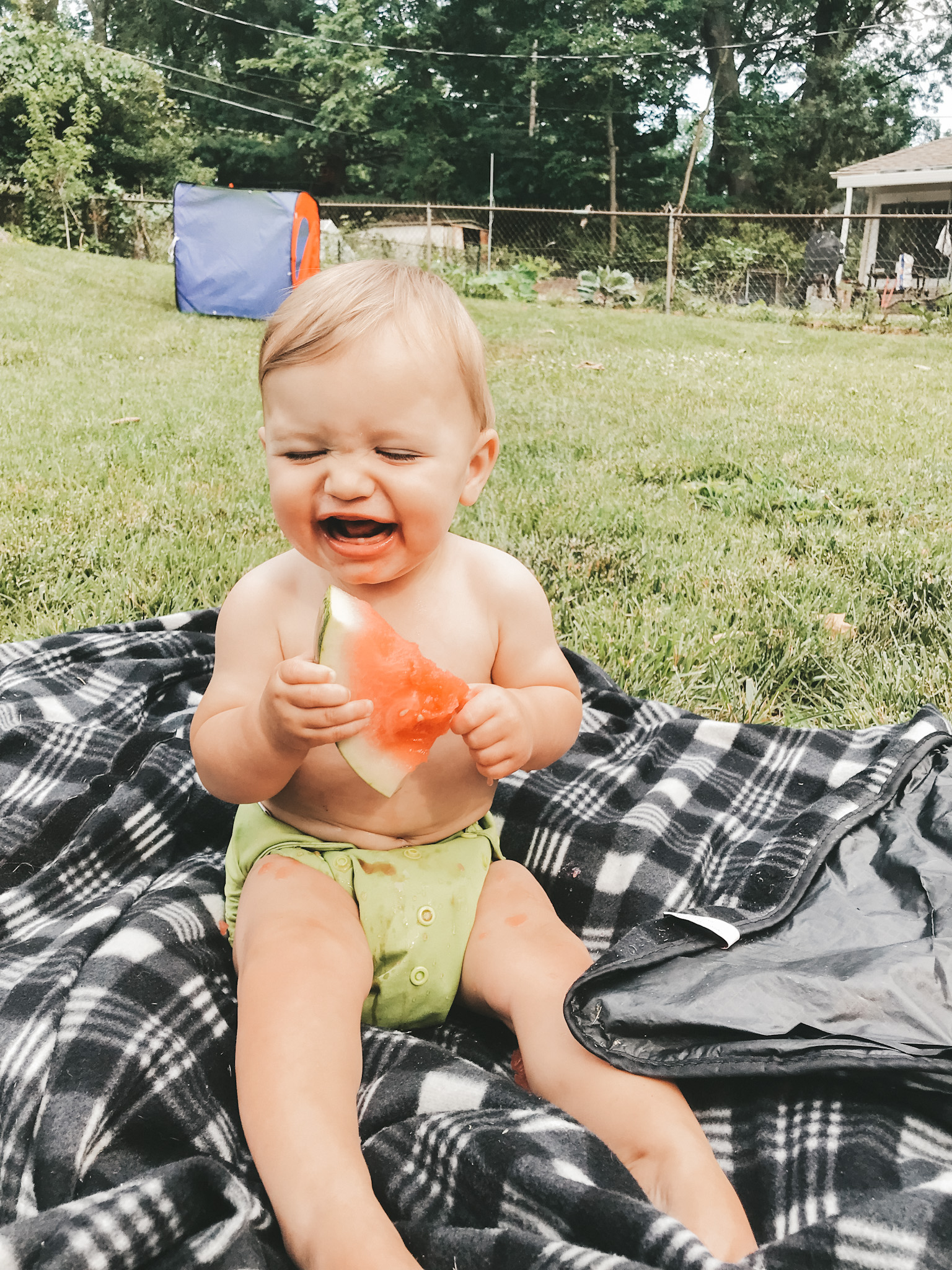 a baby holding a piece of watermelon and laughing 