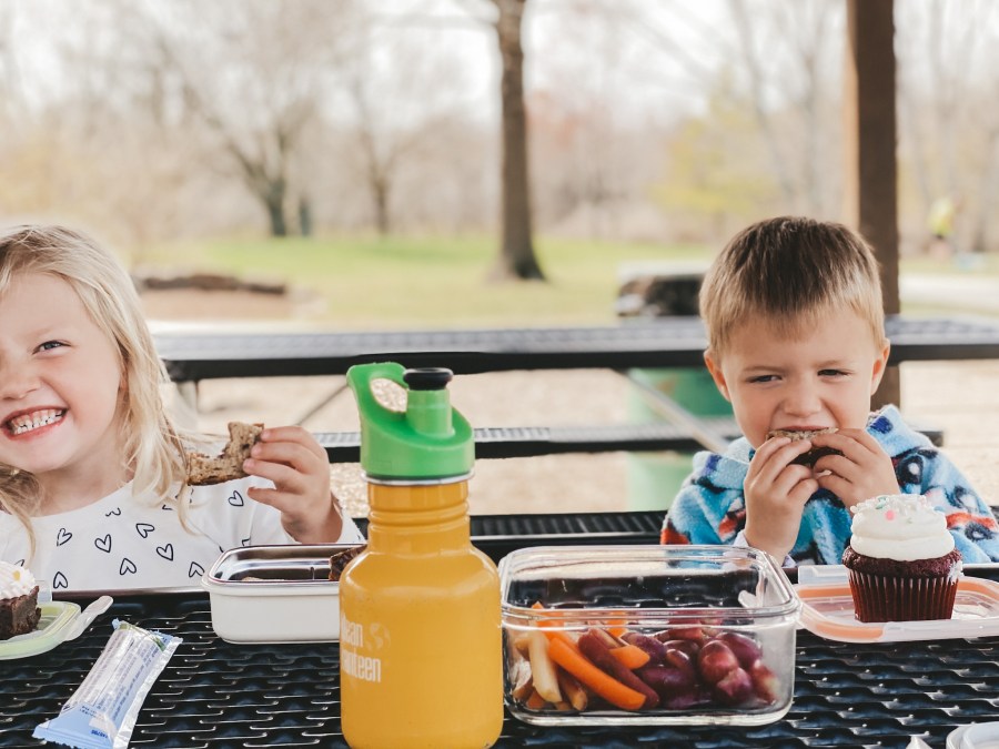 two kids sitting at a picnic table under a shelter at a park having lunch