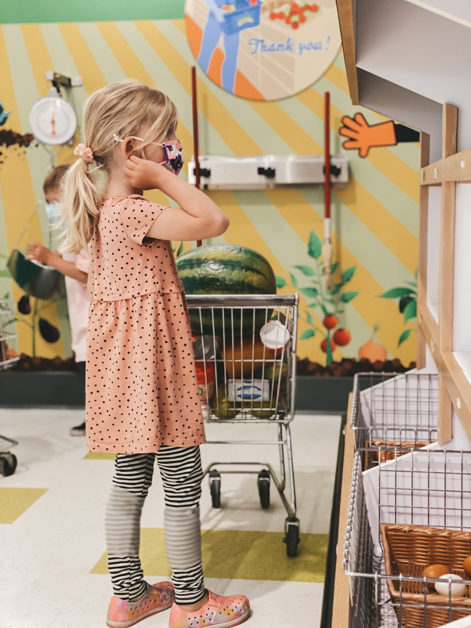 a little girl standing next to a kid-sized shopping cart in the grocery store at Wonderscope