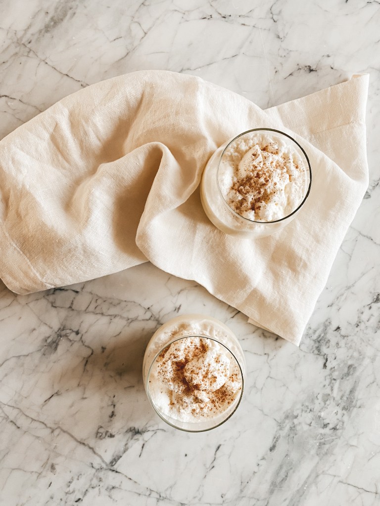 a white marble table with 2 glasses of egg nog and a beige linen napkin