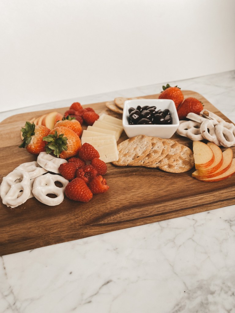 healthy valentines day snack board with fruit, cheese, and treats on a wood cutting board set on a white marble table