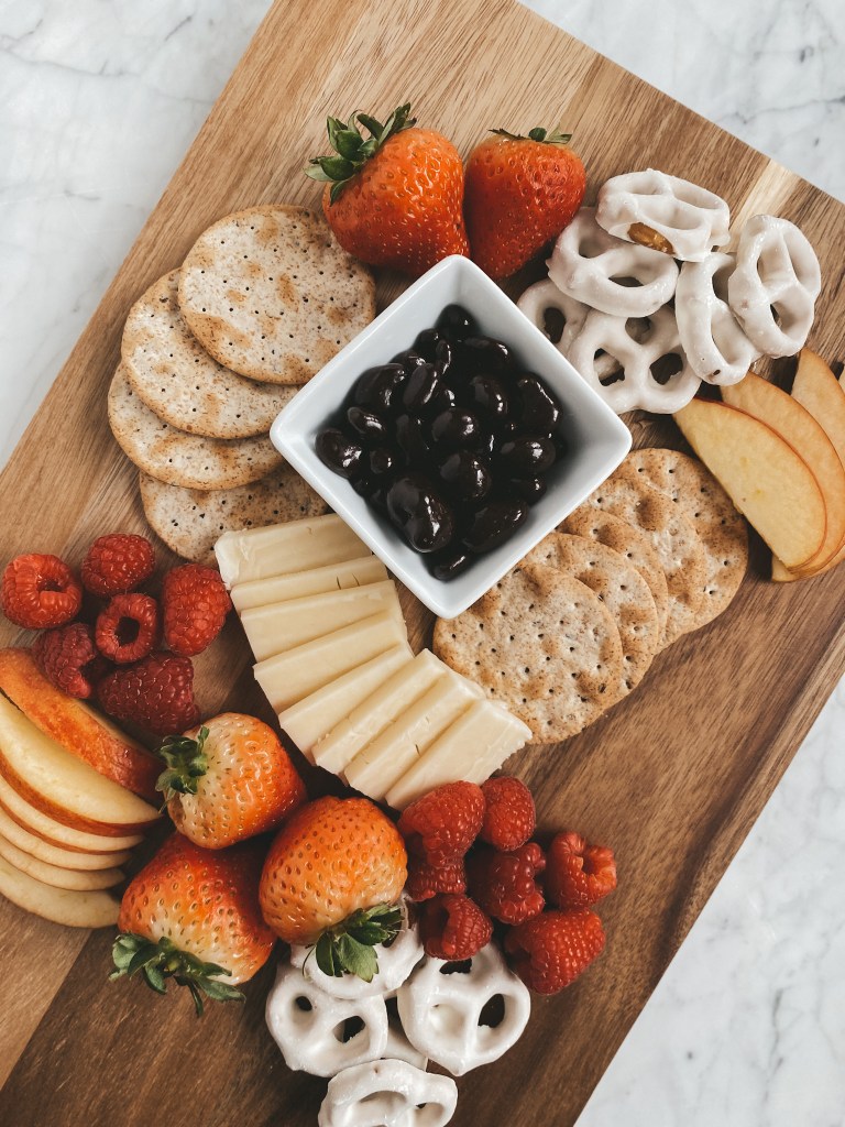 healthy valentines day snack board with fruit, cheese, and treats on a wood cutting board set on a white marble table